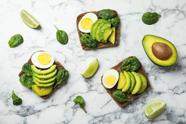 Flat lay composition with avocado toasts on white marble table — Stockfoto