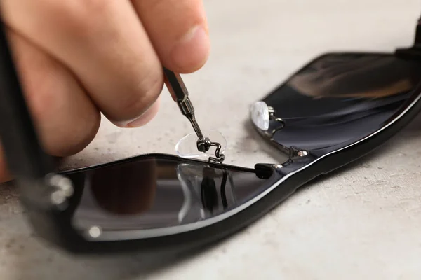 Handyman reparando óculos de sol com chave de fenda na mesa cinza, close-up — Fotografia de Stock