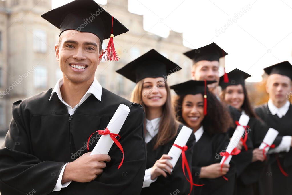 Happy students with diplomas outdoors. Graduation ceremony