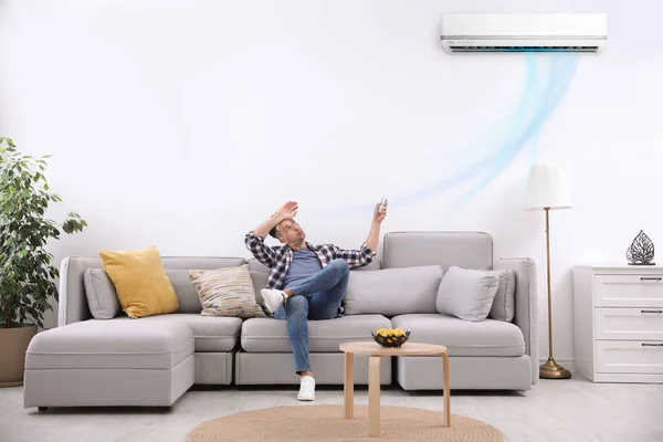 Mladý muž zapíná klimatizaci s dálkovým ovládáním doma — Stock fotografie