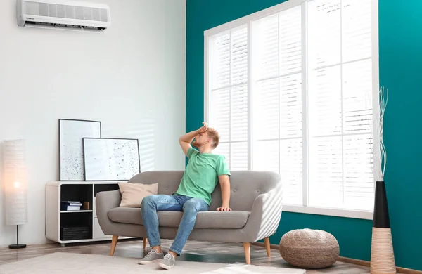 Hombre joven que sufre de calor bajo el aire acondicionado roto en casa —  Fotos de Stock