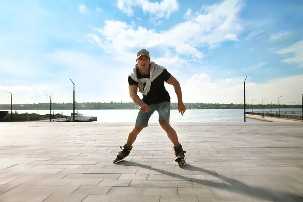 Guapo joven patinaje sobre el muelle cerca del río — Foto de Stock