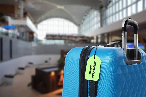 Valise bleue avec étiquette TRAVEL INSURANCE dans le terminal de l'aéroport — Photo