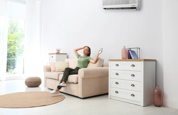 Happy young woman switching on air conditioner with remote control at home