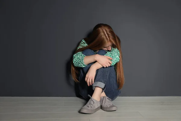 Расстроенная молодая женщина, сидящая на полу возле серой стены — стоковое фото
