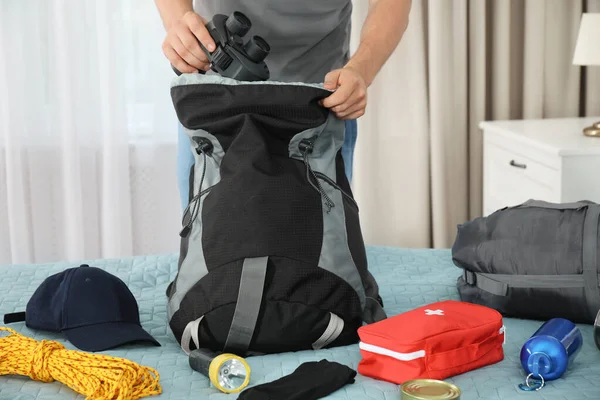 Мужчина упаковывает различные кемпинговые принадлежности в рюкзак дома, крупным планом — стоковое фото