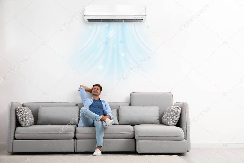 Happy young man relaxing on sofa under air conditioner at home