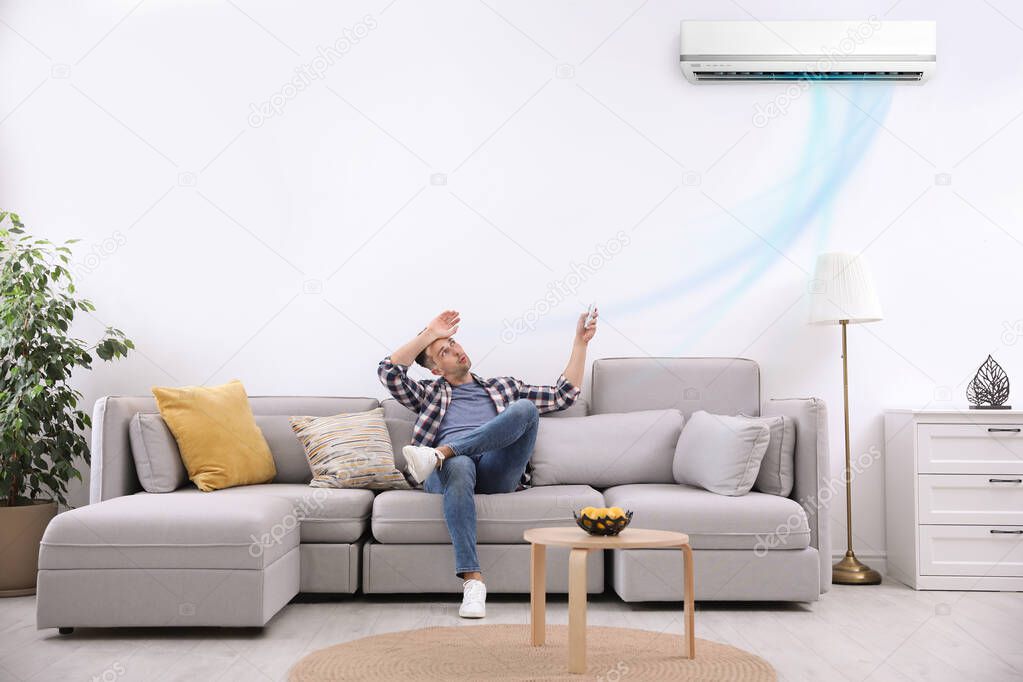 Young man switching on air conditioner with remote control at home