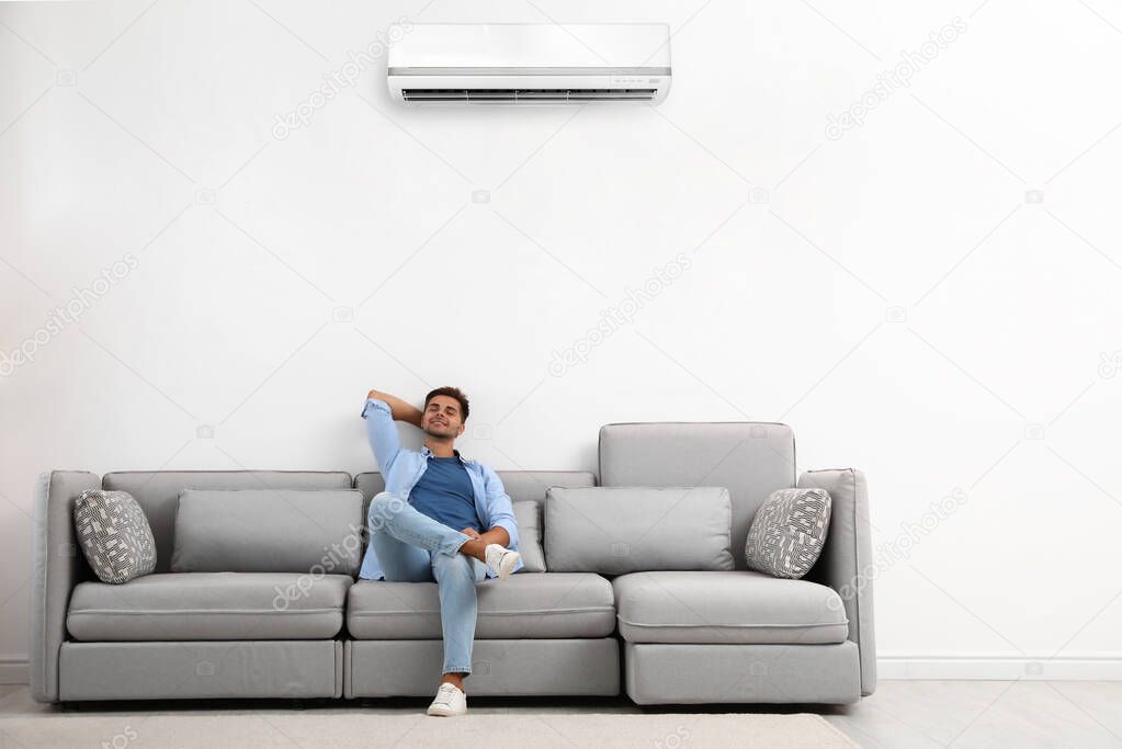 Happy young man relaxing on sofa under air conditioner at home