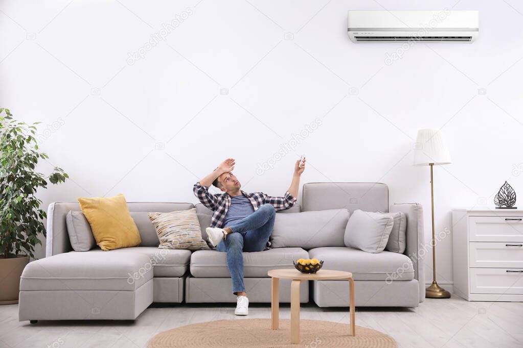 Young man switching on air conditioner with remote control at home