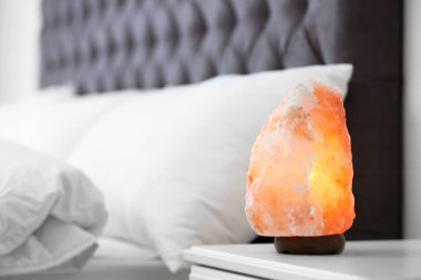 Himalayan salt lamp on table in bedroom. Space for text clipart
