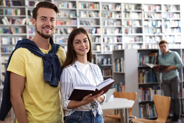 Jovens felizes com livro na biblioteca — Fotografia de Stock