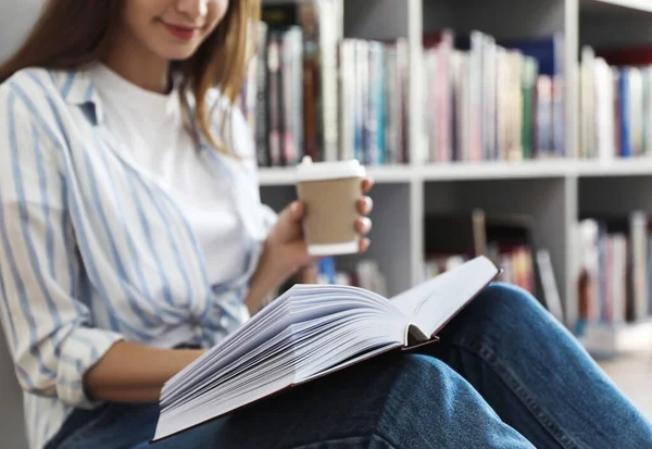 Ung kvinna med bok på golvet i biblioteket, närbild — Stockfoto