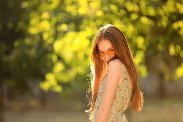 Beautiful young woman wearing sunglasses in green park — Stock Photo, Image