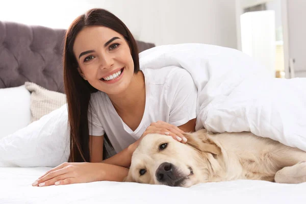 Jeune femme et son chien Golden Retriever sur le lit à la maison — Photo