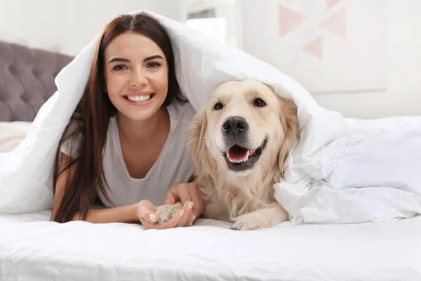 Jonge vrouw en haar Golden Retriever hond op bed thuis — Stockfoto