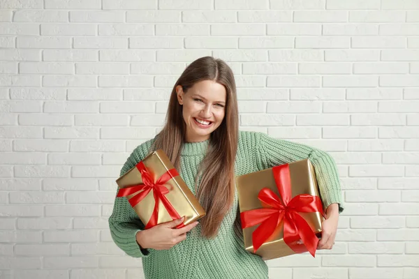 Счастливая молодая женщина с рождественскими подарками возле белой кирпичной стены — стоковое фото