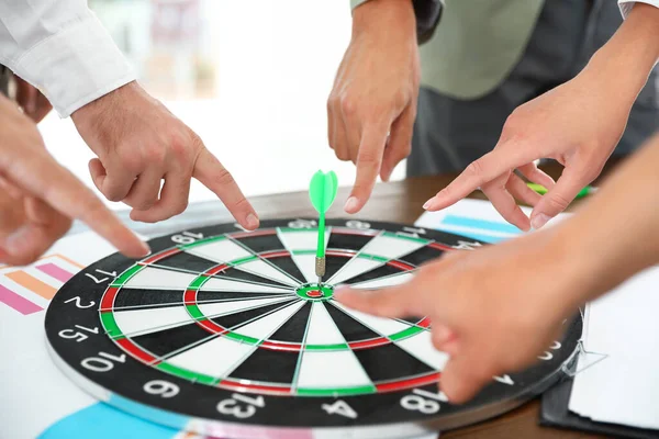 Employees pointing on dart board lying on table, closeup