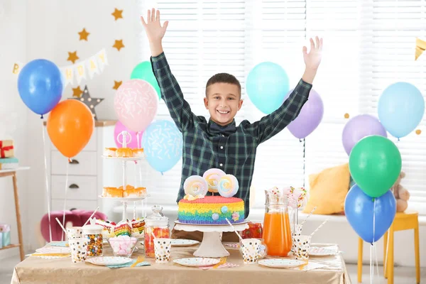 Happy boy at table with treats in room decorated for birthday party — Stock Photo, Image