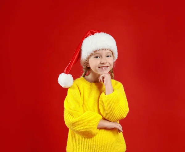 Мила маленька дитина в капелюсі Санта на червоному тлі. Різдвяні свята — стокове фото