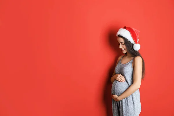 Mulher grávida feliz vestindo chapéu de Papai Noel para a festa de Natal em fundo vermelho, espaço para texto. Bebê esperado — Fotografia de Stock