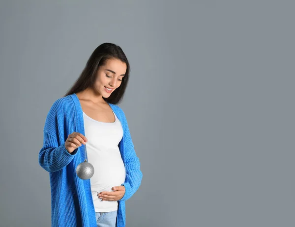 Mulher grávida feliz com bola de Natal em fundo cinza, espaço para texto. Bebê esperado — Fotografia de Stock