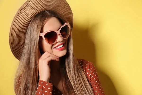 Młoda kobieta nosi stylowe okulary przeciwsłoneczne i kapelusz na żółtym tle — Zdjęcie stockowe