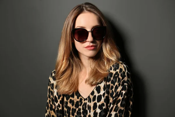 Junge Frau mit stylischer Sonnenbrille auf dunkelgrauem Hintergrund — Stockfoto