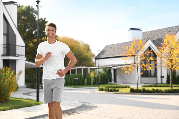 Hombre joven con auriculares corriendo al aire libre en la mañana soleada. Estilo de vida saludable — Foto de Stock