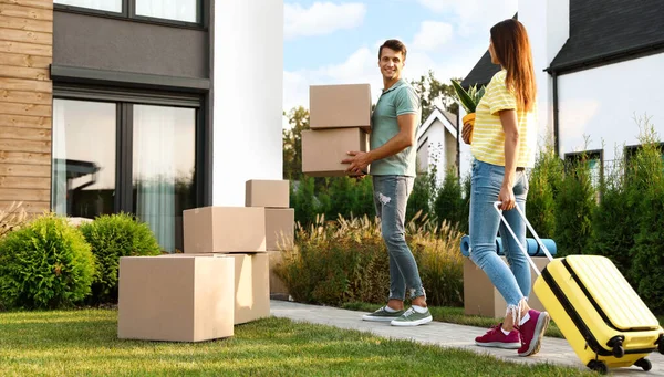 Couple walking to their new house with moving boxes and household stuff