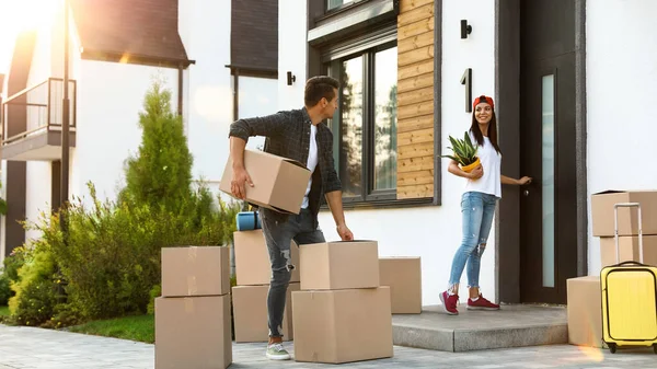 Happy couple with moving boxes and household stuff near their new house on sunny day