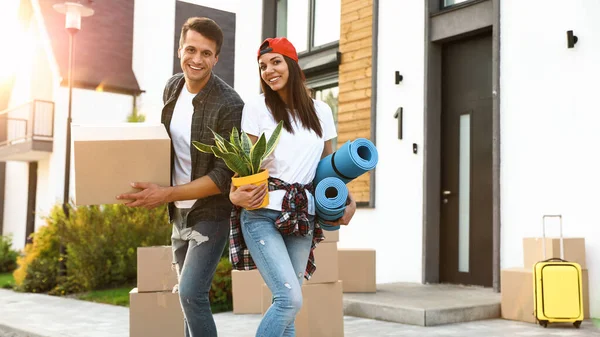 Happy couple with moving boxes and household stuff near their new house on sunny day