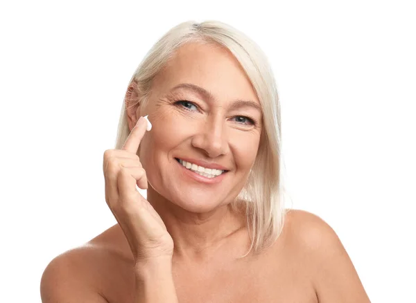 Mujer madura aplicando crema facial sobre fondo blanco —  Fotos de Stock