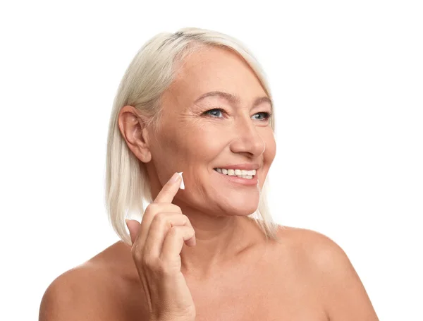 Mujer madura aplicando crema facial sobre fondo blanco —  Fotos de Stock