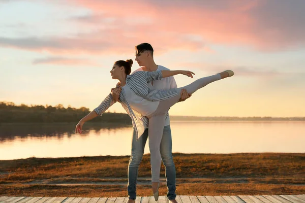 Hermosa pareja joven practicando movimientos de baile cerca del río al atardecer — Foto de Stock