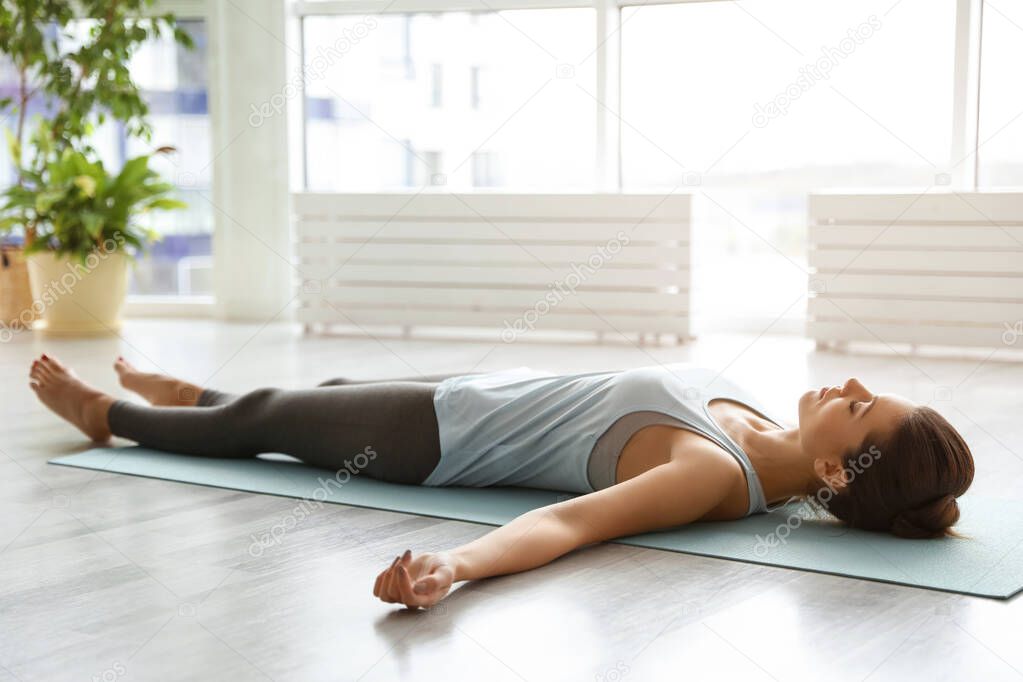 Young woman practicing corpse asana in yoga studio. Savasana pose