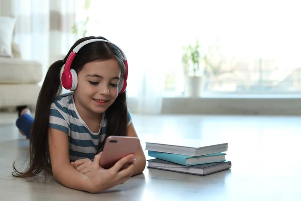 Cute Little Girl Słuchawkami Smartfon Słuchając Audiobook Domu — Zdjęcie stockowe