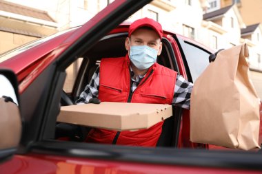 Koruyucu maskeli bir kurye ve arabadan inme emri almış eldivenler. Coronavirus karantinası sırasında yiyecek teslimatı