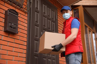 Koruyucu maskeli bir kurye ve evin girişinde kutusu olan eldivenler. Coronavirus karantinası sırasında teslimat servisi