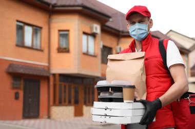 Koruyucu maskeli ve eldivenli bir kurye evin yakınlarında sipariş vermiş. Coronavirus karantinası sırasında yiyecek teslimatı