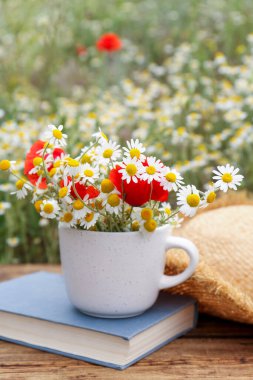 Papatya çayı, haşhaş, hasır şapka ve açık hava masasında kitap kompozisyonu