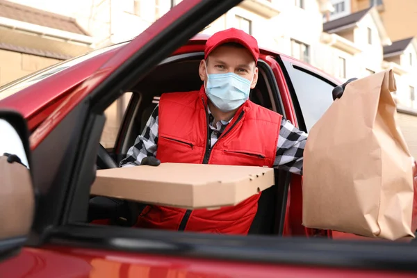 Koruyucu maskeli bir kurye ve arabadan inme emri almış eldivenler. Coronavirus karantinası sırasında yiyecek teslimatı