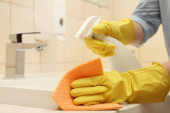 Nő tisztító mosogató mosószerrel és rongy a fürdőszobában, közelkép