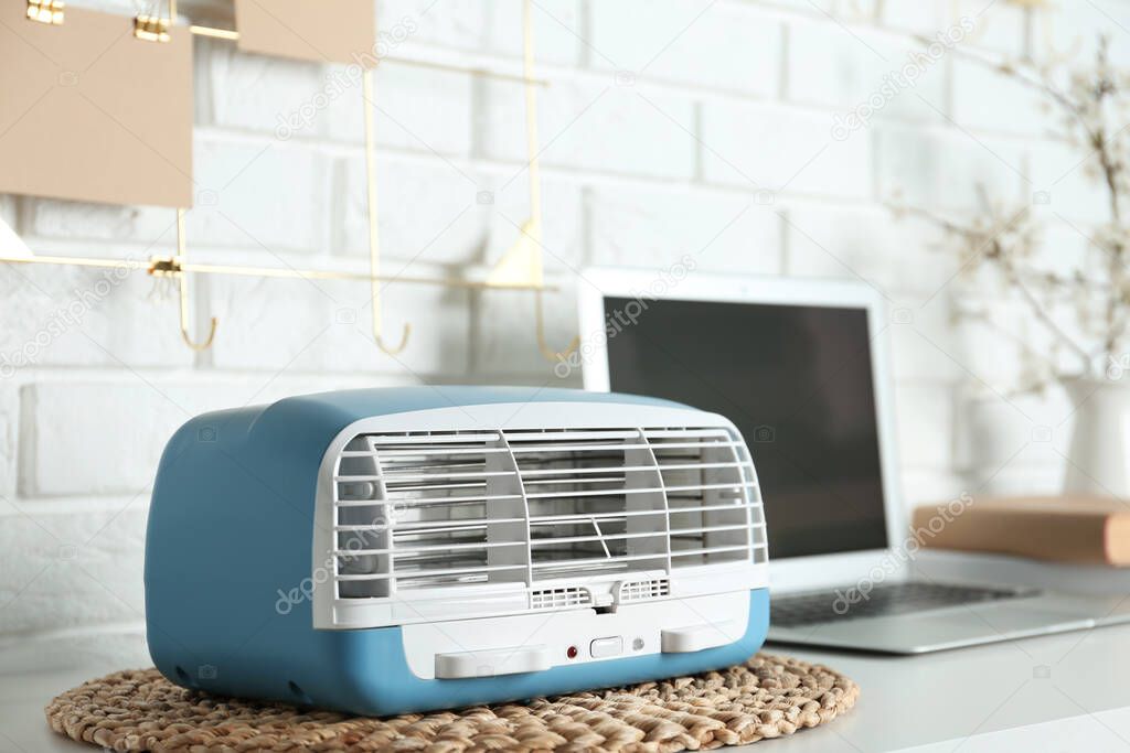 Modern air purifier near laptop on white wooden table in room