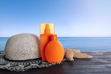 Deniz kenarındaki ahşap masada güneş koruma ürünleri ve şık şapkalar. Metin için boşluk