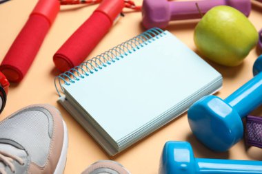 Turuncu zemin üzerinde fitness ekipmanı, defter ve elma kompozisyonu