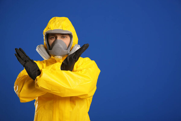 Man in chemical protective suit making stop gesture on blue background, space for text. Virus research