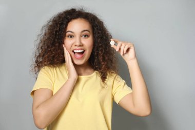 Açık gri arka planda vitamin hapı olan duygusal Afro-Amerikalı kadın.