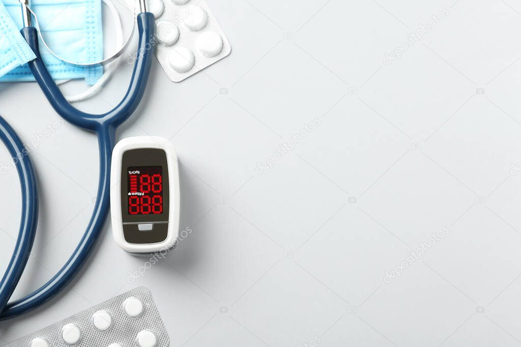 Flat lay composition with modern fingertip pulse oximeter and medical items on white background. Space for text