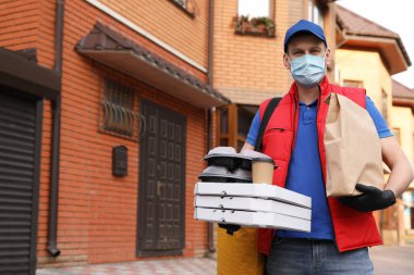 Koruyucu maskeli ve eldivenli bir kurye evin yakınlarında sipariş vermiş. Coronavirus karantinası sırasında yiyecek teslimatı
